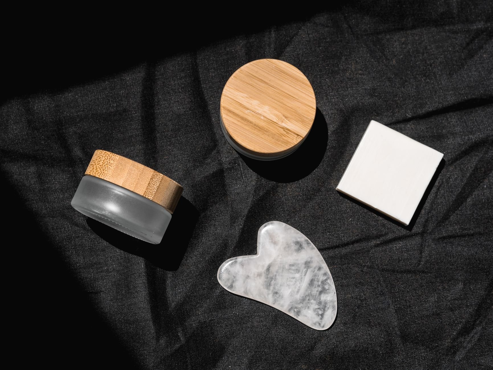 Flat lay of skincare products on dark fabric — gua sha stone and beauty containers.