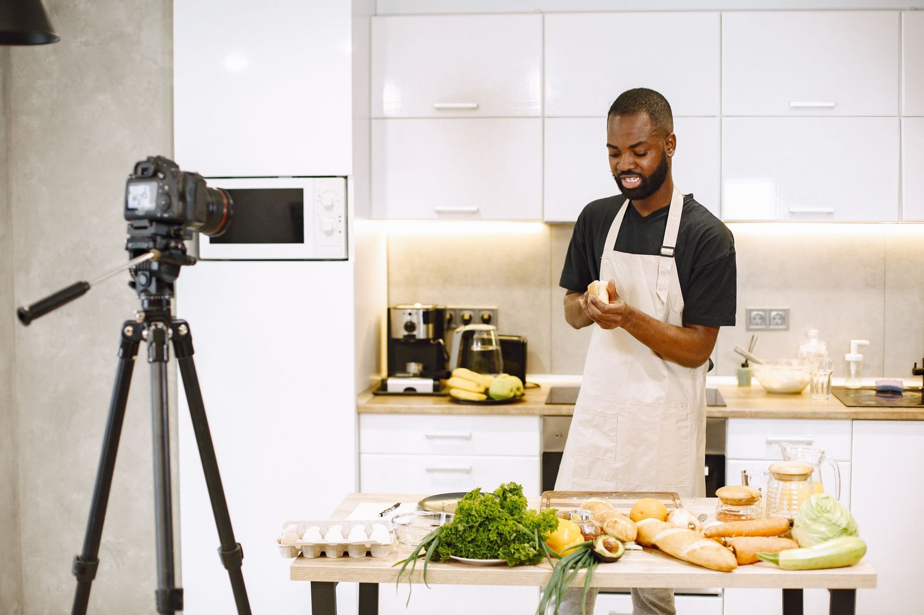 A man prepares food in a kitchen while recording a cooking video.